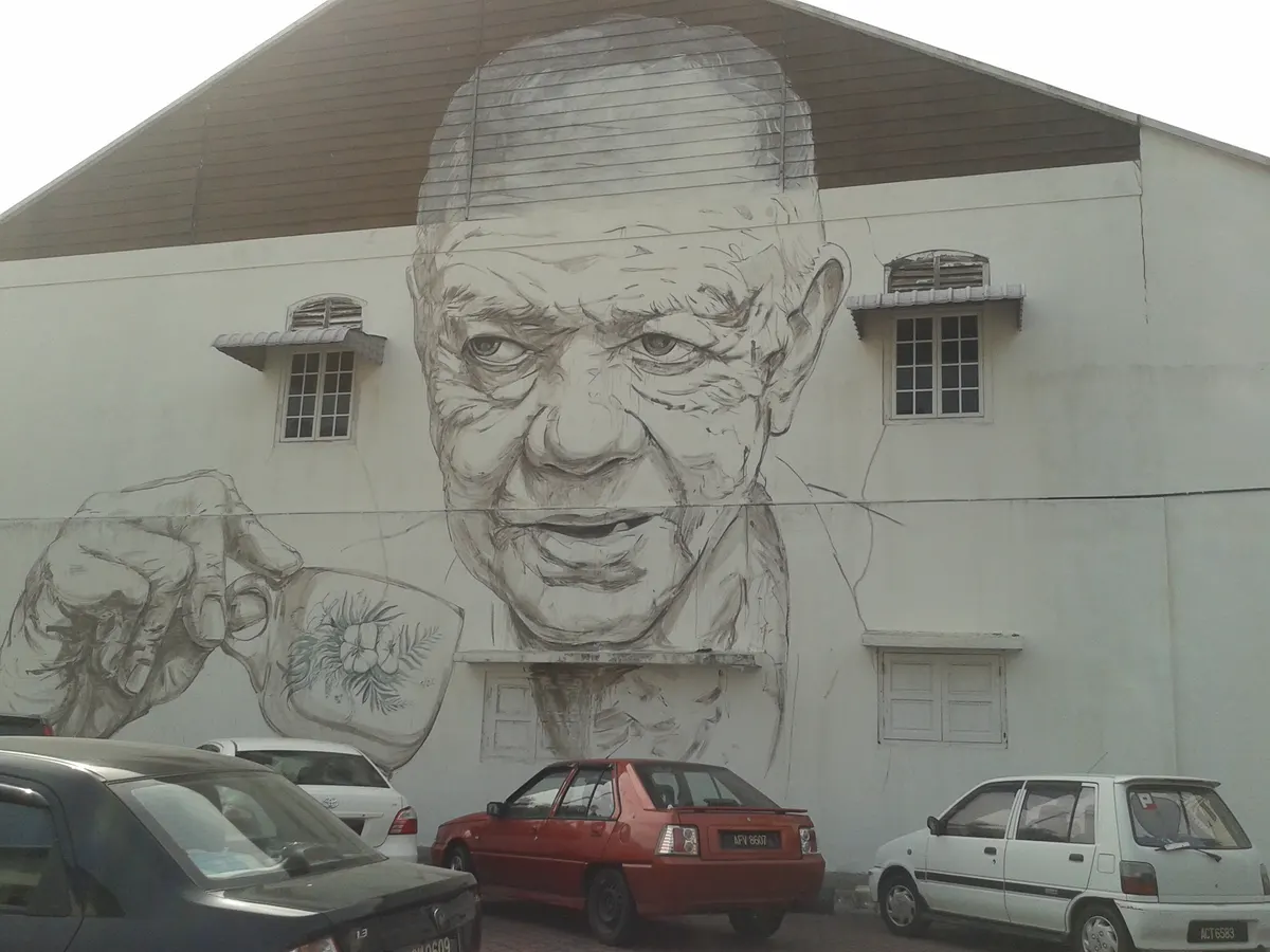 A large black and white mural of an old man on a wall in Ipoh old town