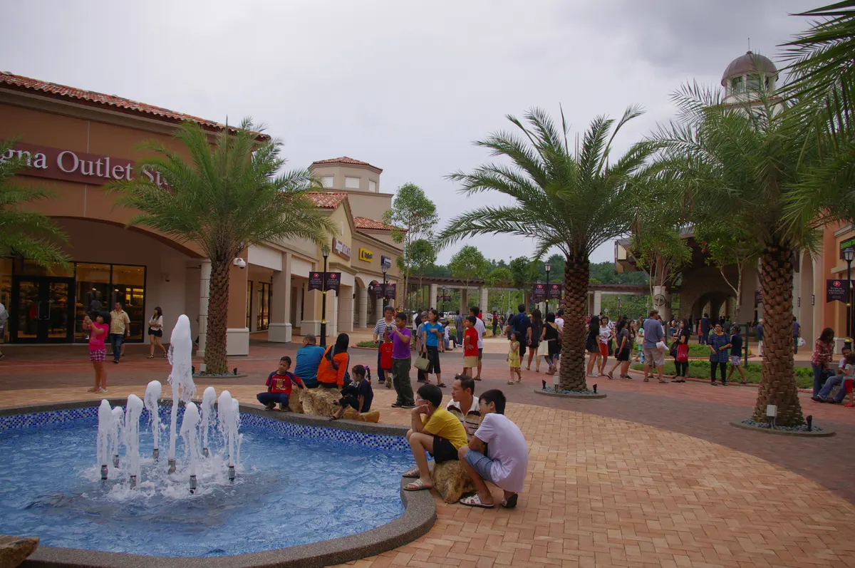 The open-air shopping village at Johor Premium Outlets with a fountain and palm trees