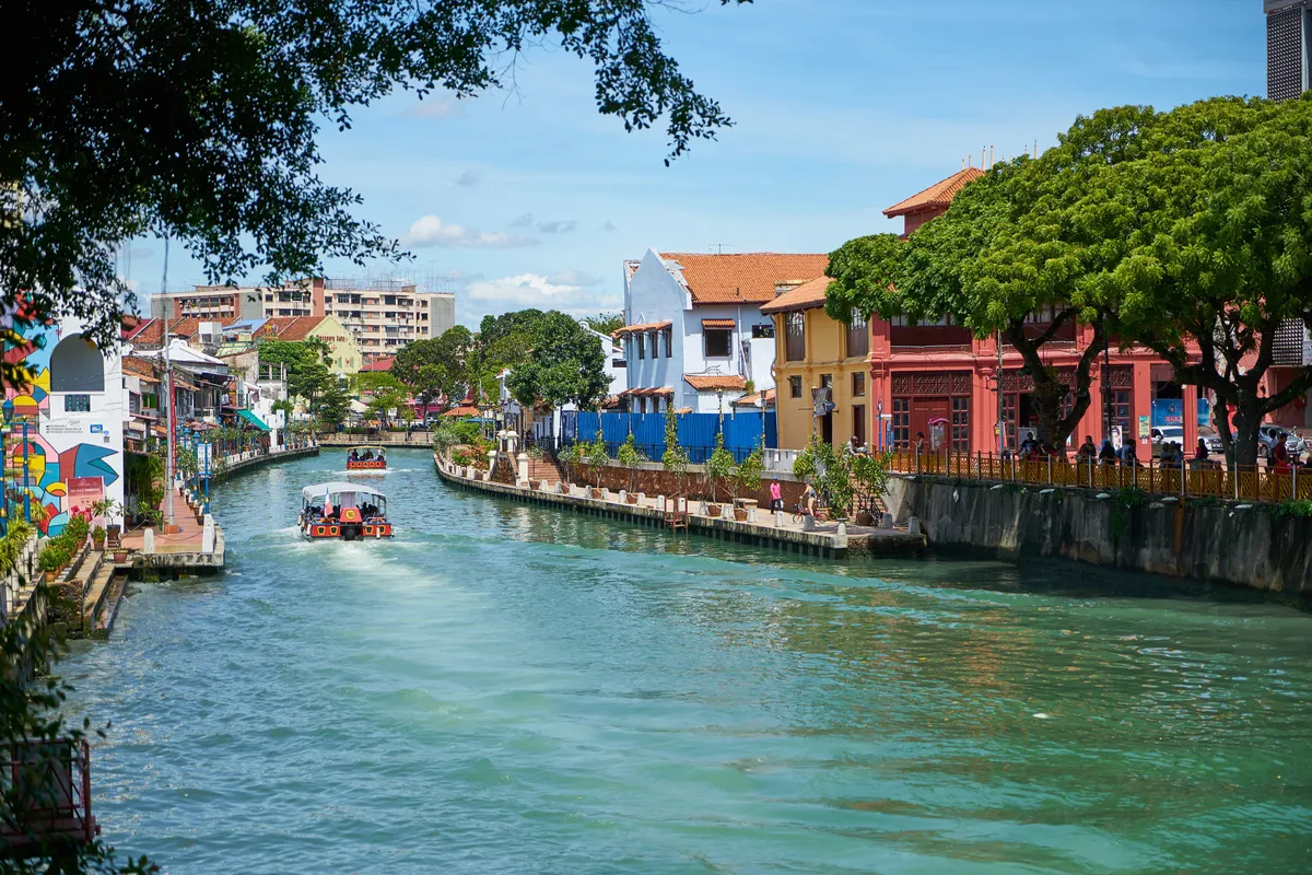 A river cruise boat on the Melaka River between colourful riverside buildings